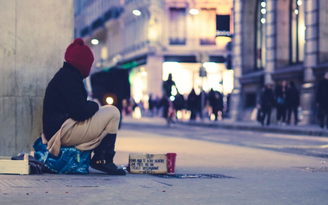 A homeless person sits next to a wall in a city centre