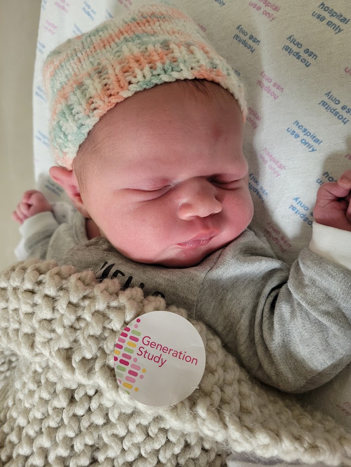 A picture of Sophia Bird laid on a hospital bed beneath a blanket with a sticker which reads 'Generation Study.'