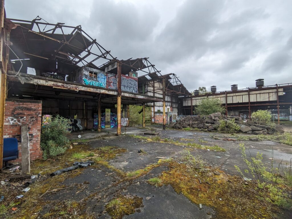 Overgrown derelict factory building with graffiti and a large pile of rubble