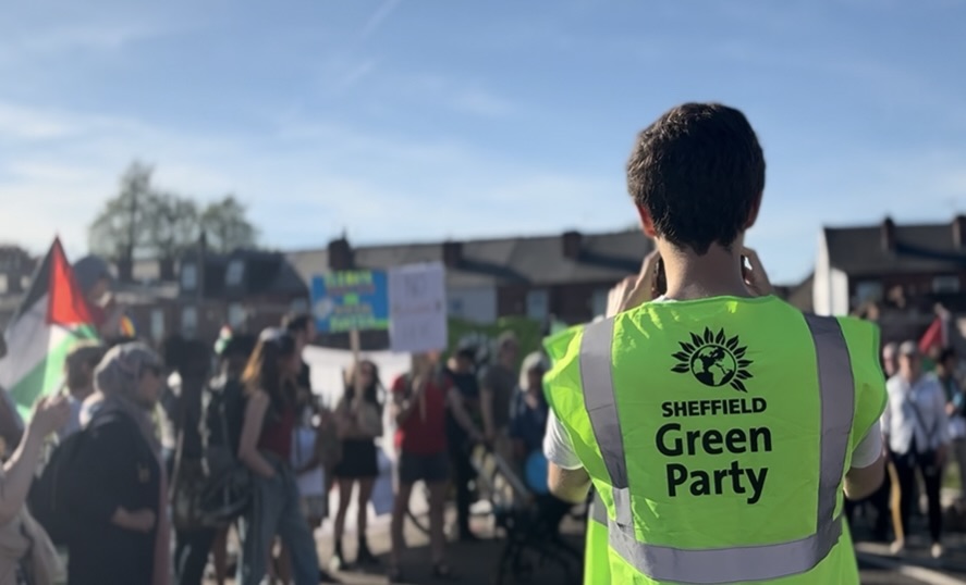 Member of Sheffield Green Party in neon green vast facing protestors