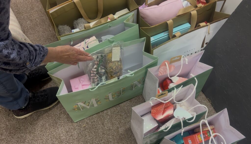 Hand reaching into a bag labelled "Mum" surrounded by other similar bags.