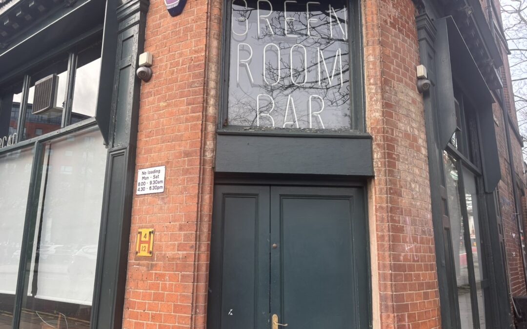 The outside of a bar called the greenroom in sheffield city centre with a green door and neon lighting