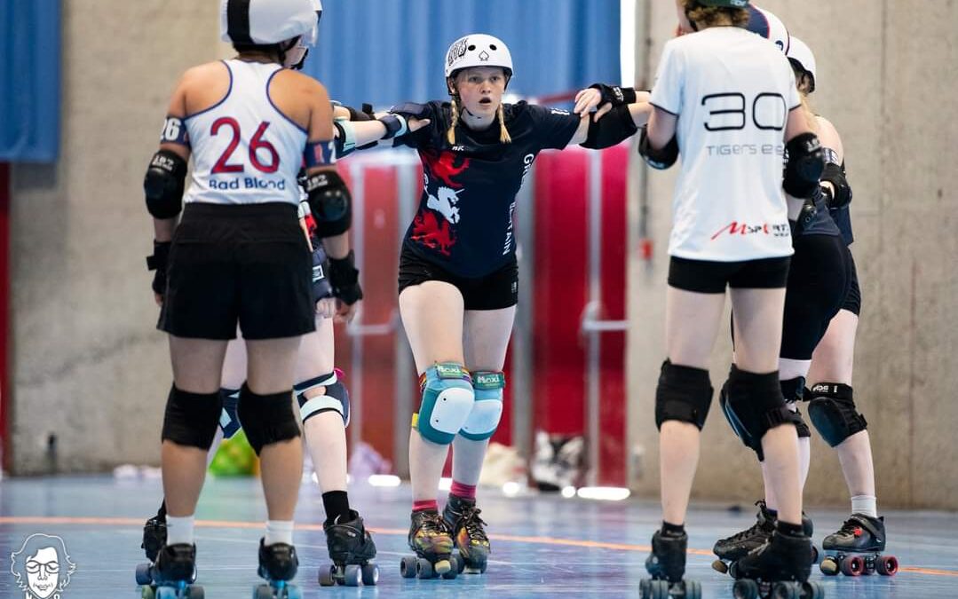 A girl in roller skates, knee pads and a helmet looking ahead surrounded by other women during a game roller derby