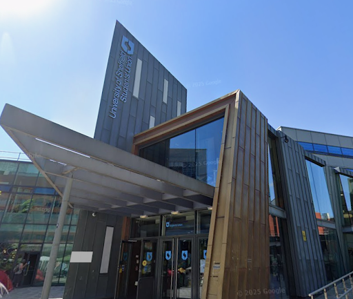 Entrance to a large, modern building mostly made of glass, with a large sign above saying ‘University of Sheffield Students Union’