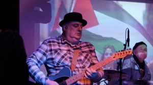 Blues guitarist playing on stage with Palestinian flag in the background