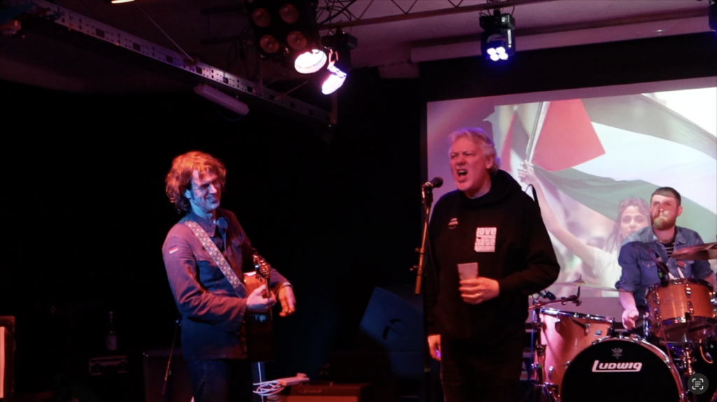 Event organiser introducing a band on stage with a blues band in the background