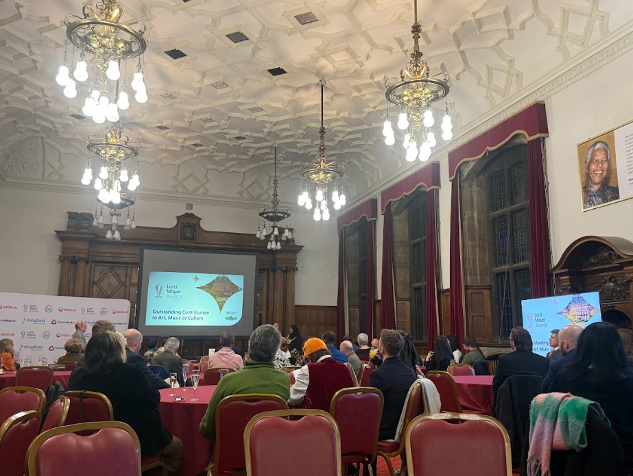 The room in Sheffield Town Hall where the Lord Mayor Awards are taking place. Round tables with people sat around them. Facing a scteen. 