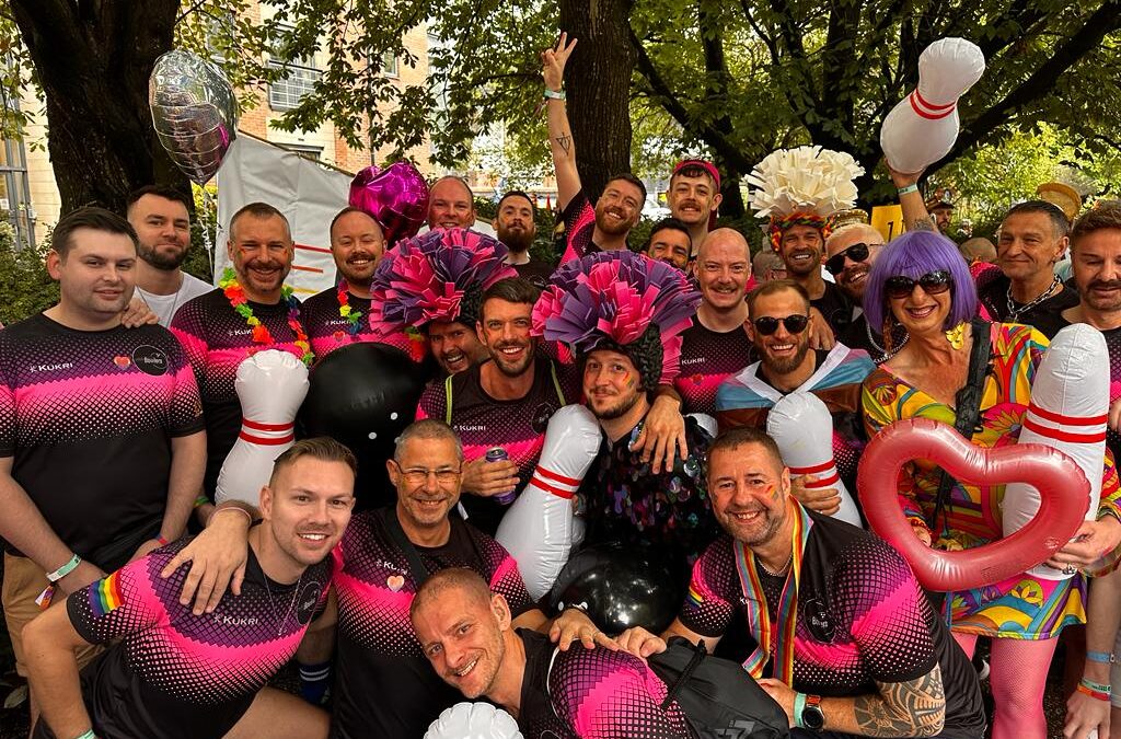 A Gay City Bowlers group outside huddled together, with inflatable bowling pins and balloons.