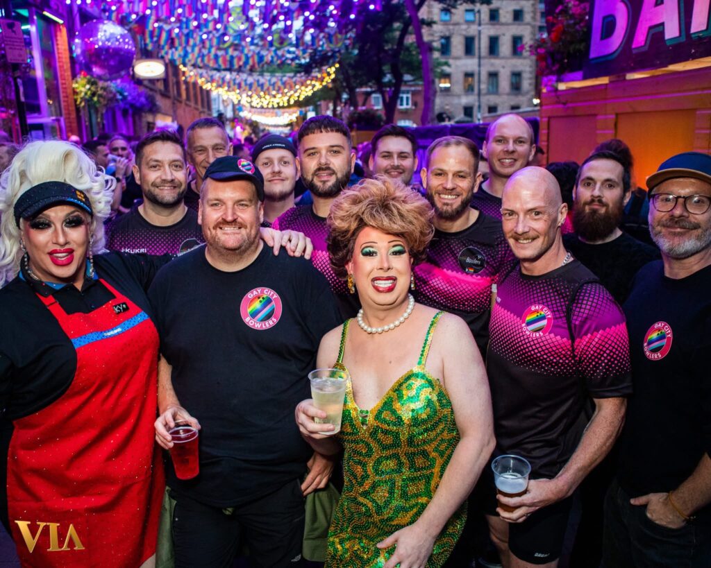 A Gay City Bowlers group including drag queens at a bowling event posing together.