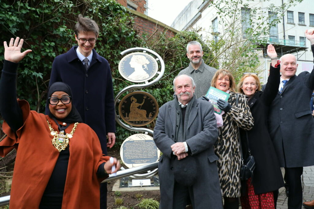 Members of the council and sculptor surrounding the sculpture with their arms in the air