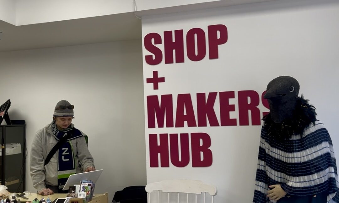 Inside a store with an employee at the till and the sign "SHOP + MAKERS HUB" on the wall.