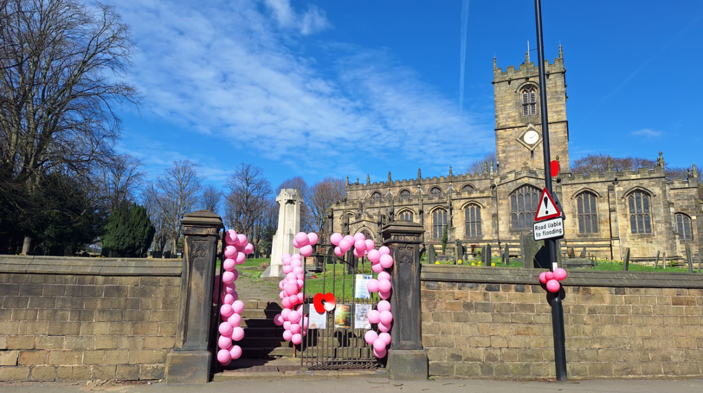 An image of Ecclesfield church, with pink balloons tied to the gates and lamppost near by.