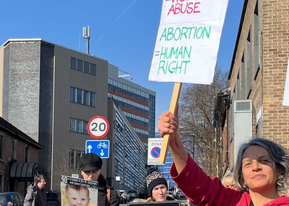 A counter-protestor stood in front of anti-abortionist protestors. She is holding a sign that says abortion is a human right.