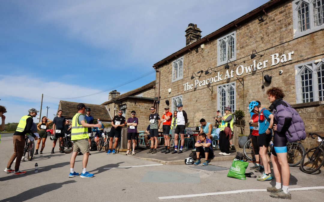 A crowd of athletes by their bikes outside of the Peacock at Owler Bar.