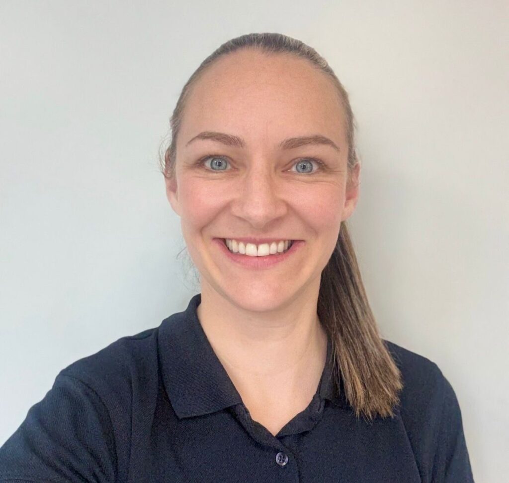 A woman smiling with her teeth in a navy polo shirt 