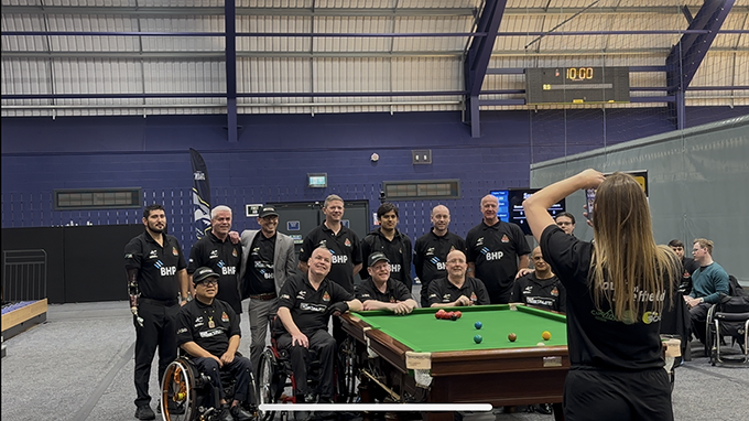 Players pose for a group photo behind 10 Cue snooker table