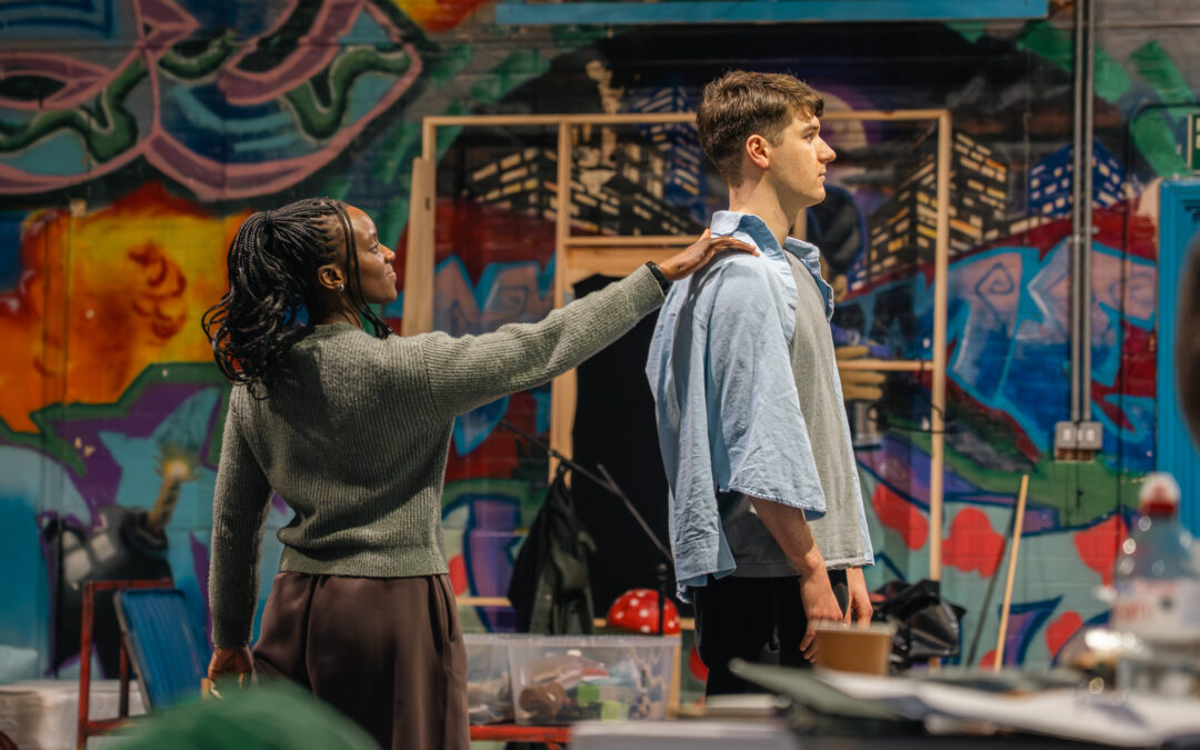 Image of Brianna Douglous putting her hand on Lewis Tidy's shoulder from behind. In rehersals