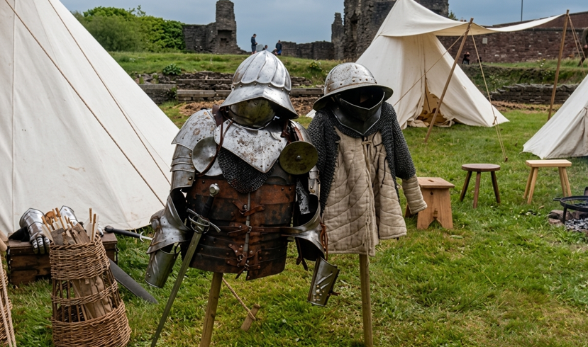 Two armour stands in front of a tent, both covered with medieval armour. One has a sword