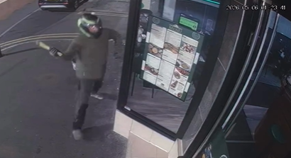 Photo of a man smashing up the windows of a turkish restaurant. he is wearing a bike helmet and a dark green coat.