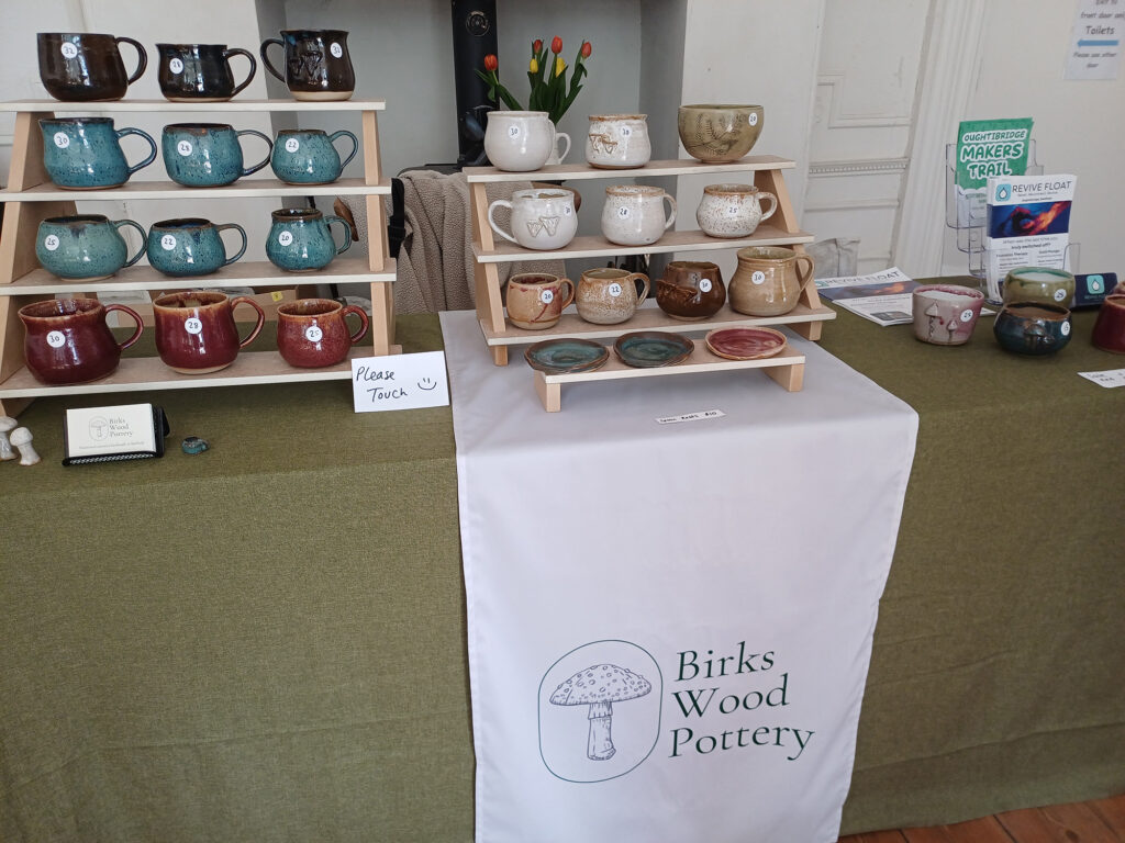 mugs on stands at the exhibition with a sign saying 'please touch'
