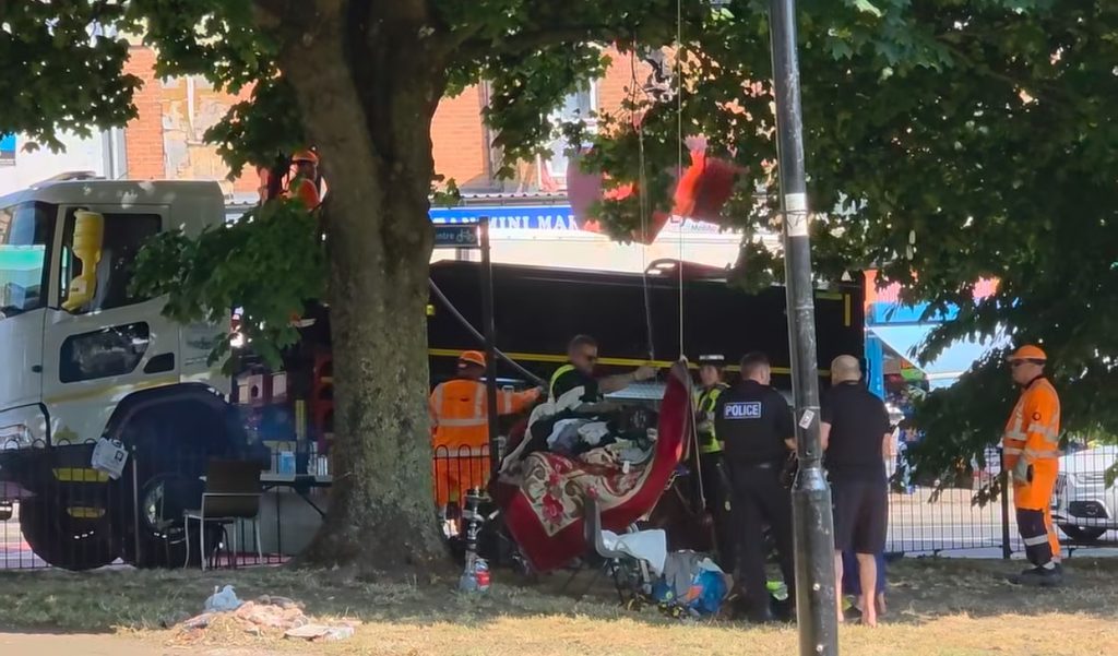 Police and council workers removing the camp, onto the back of a pickup lorry. People are seen in orange hi-vis, and police officers.